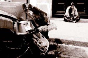 Sad woman sitting next to her damaged car.